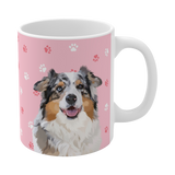 Close up of pink ceramic mug with paws pattern, featuring a smiling, multicolored Australian Shepherd [LightPinkPawsHandIllustration]