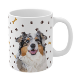 Close up of white ceramic mug with paws and bones pattern, featuring a smiling, multicolored Australian Shepherd [PawsandBonesHandIllustration]