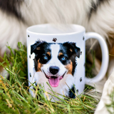 White mug in tall grass featuring a smiling Australian Shepherd illustration.