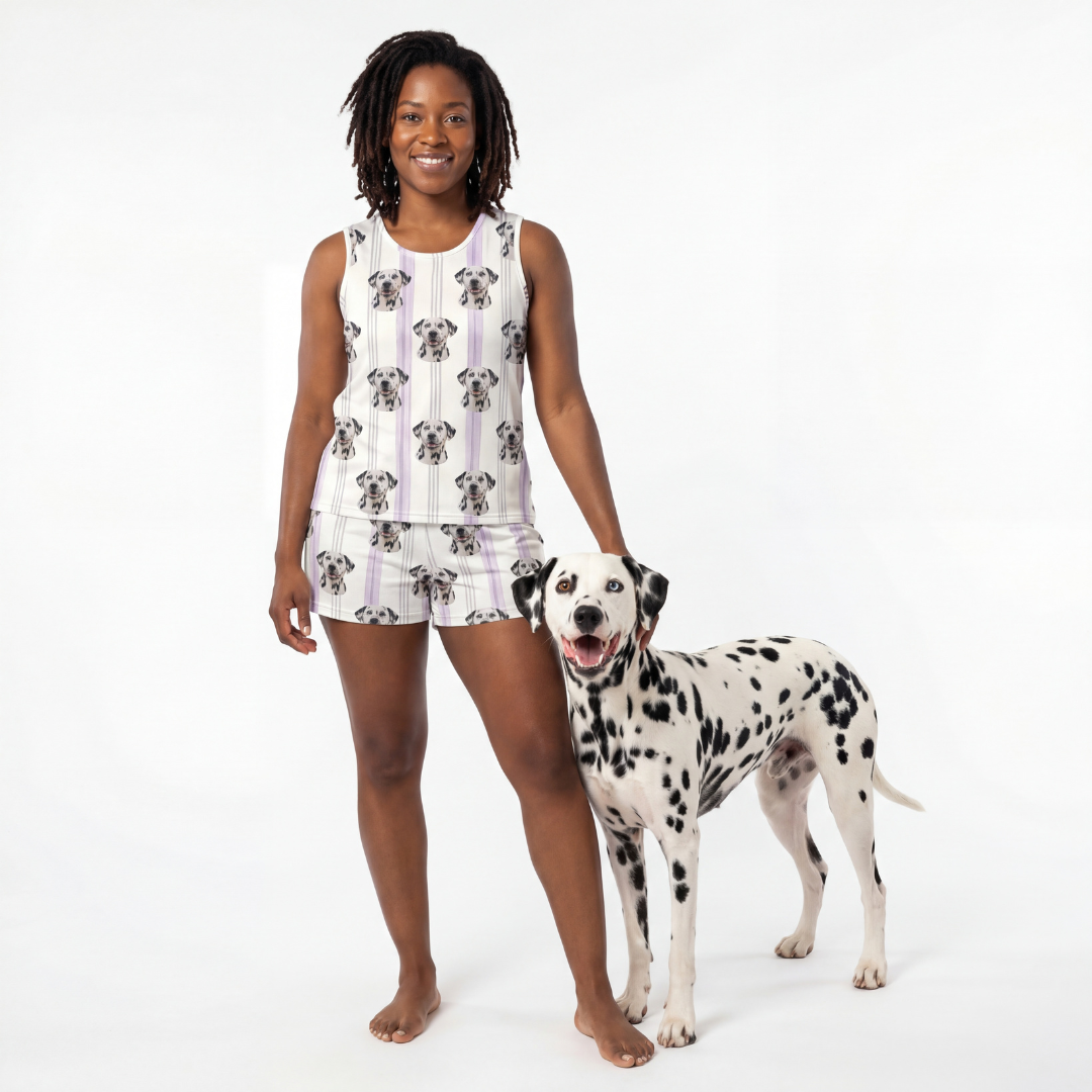 Woman wearing a sleeveless top and shorts with a dalmatian pattern, standing next to a dalmatian dog on a white background.