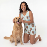 Woman wearing tank top pajamas set kneeling next to a golden dog on a white background